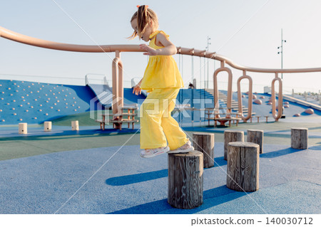 Little girl balancing on playground stumps, focused and playing on a sunny day. Little girl balancing on playground stumps, focused and playing on a sunny day. 140030712