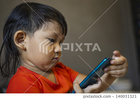 Toddler Using Smartphone To Call His Mother In The Room. Cute asian little boy pretending to make a phone call to his mom, ideal for family lifestyle, technology and childhood development themes. Toddler Using Smartphone To Call His Mother In The Room. Cute asian little boy pretending to make a phone call to his mom, ideal for family lifestyle, technology and childhood development themes. 140031321