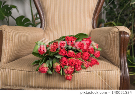Vibrant red tulips resting on an elegant armchair in a cozy indoor setting Vibrant red tulips resting on an elegant armchair in a cozy indoor setting 140031584