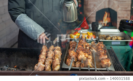 Male caucasian grilling kebabs outdoors near cozy fireplace in winter setting Male caucasian grilling kebabs outdoors near cozy fireplace in winter setting 140031588