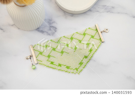 Green beaded bracelet with geometric pattern on marble surface Green beaded bracelet with geometric pattern on marble surface 140031593