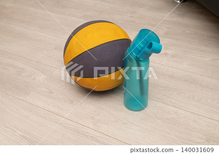 Yellow basketball and blue water bottle on wooden floor Yellow basketball and blue water bottle on wooden floor 140031609