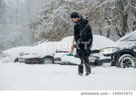 Individual in black winter coat shoveling snow in a parking lot covered in snow with parked cars partially obscured by snow during a winter storm Individual in black winter coat shoveling snow in a parking lot covered in snow with parked cars partially obscured by snow during a winter storm 140031672