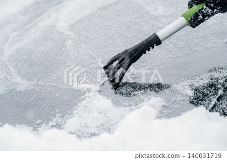Snow removal tool is scraping ice off a car windshield covered in snow during winter weather, demonstrating the need for maintenance in cold conditions Snow removal tool is scraping ice off a car windshield covered in snow during winter weather, demonstrating the need for maintenance in cold conditions 140031719