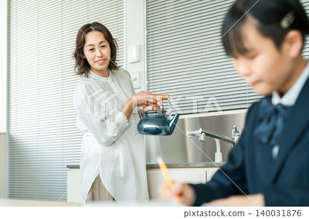 一個穿著制服的女孩在學習，一位母親在做家事時看著女兒學習 140031876