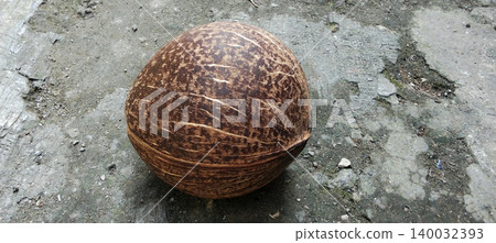 Close-up photo of a natural brown coconut shell with a unique texture placed on a rough ground surface. Close-up photo of a natural brown coconut shell with a unique texture placed on a rough ground surface. 140032393