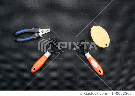 Grooming tools for dogs including a slicker brush, comb, and nail clippers arranged on a textured black surface for pet care and maintenance Grooming tools for dogs including a slicker brush, comb, and nail clippers arranged on a textured black surface for pet care and maintenance 140032503
