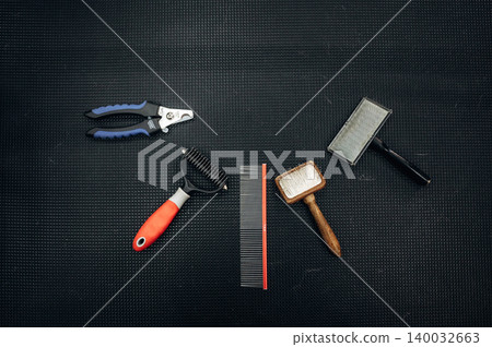 Grooming tools for dogs displayed on a textured black surface, including combs, brushes, and clippers arranged for easy access during pet grooming sessions 140032663