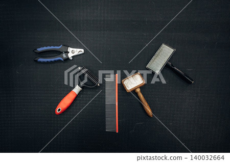 Grooming tools for dogs arranged on a black textured surface, including combs, brushes, and clippers for effective pet care and maintenance 140032664