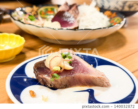 Straw-grilled bonito tataki is a specialty dish from Kochi Prefecture, Japan. It's a dish of seared bonito sashimi eaten with condiments. One slice on a plate. Straw-grilled bonito tataki is a specialty dish from Kochi Prefecture, Japan. It's a dish of seared bonito sashimi eaten with condiments. One slice on a plate. 140032872