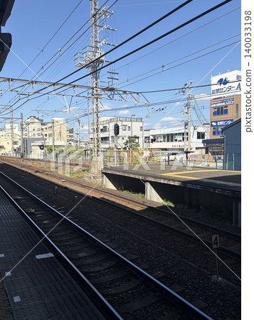 A view of the Nankai Electric Railway station platform and double tracks under a clear blue sky. A view of the Nankai Electric Railway station platform and double tracks under a clear blue sky. 140033198