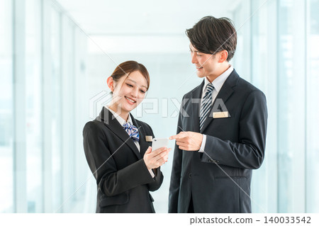 A businessman and woman in suits talking while looking at their smartphones (communication) A businessman and woman in suits talking while looking at their smartphones (communication) 140033542