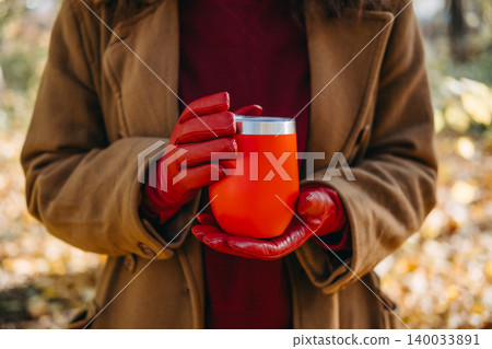 Person holds reusable beverage container in hands while standing in forest. Cozy hot drink outdoor comfort, winter transition seasonal marketing, warm beverage warming up hands. Person holds reusable beverage container in hands while standing in forest. Cozy hot drink outdoor comfort, winter transition seasonal marketing, warm beverage warming up hands. 140033891
