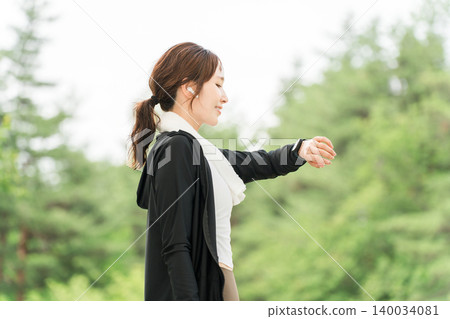 A woman using a smartwatch while exercising (healthcare, music, workout). 140034081