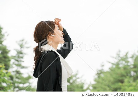 A woman wearing earphones while running, walking, jogging, or exercising in a park (dieting, sports) A woman wearing earphones while running, walking, jogging, or exercising in a park (dieting, sports) 140034082