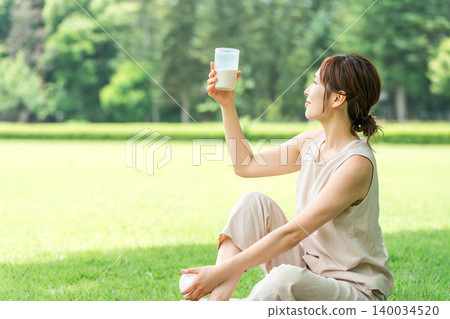 A woman's profile as she drinks protein while doing yoga in the forest. A woman's profile as she drinks protein while doing yoga in the forest. 140034520