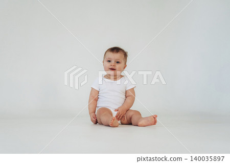 Baby sitting on a plain white background wearing a short-sleeved white onesie, with a neutral expression and bare feet, showcasing a simple and clean aesthetic Baby sitting on a plain white background wearing a short-sleeved white onesie, with a neutral expression and bare feet, showcasing a simple and clean aesthetic 140035897