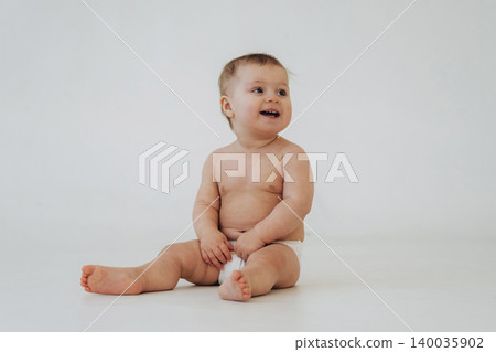 Baby sitting on a white background, wearing only a diaper, smiling and looking to the side, showcasing soft skin and chubby limbs in a bright, minimalistic setting Baby sitting on a white background, wearing only a diaper, smiling and looking to the side, showcasing soft skin and chubby limbs in a bright, minimalistic setting 140035902