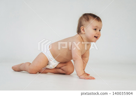 Baby crawling on hands and knees wearing a diaper, smiling with light brown hair against a plain white background in a well-lit indoor setting Baby crawling on hands and knees wearing a diaper, smiling with light brown hair against a plain white background in a well-lit indoor setting 140035904