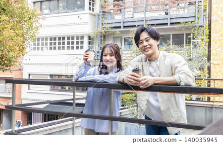 一男一女面帶微笑地坐在露臺上，手裡拿著咖啡。 140035945