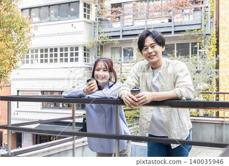 一男一女面帶微笑地坐在露臺上，手裡拿著咖啡。 140035946