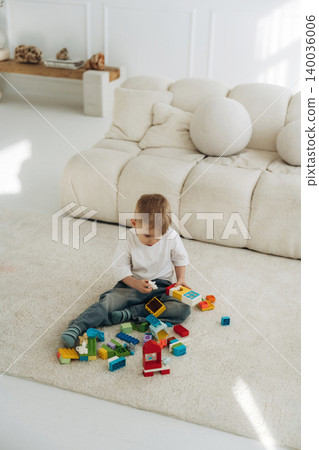 Young boy playing with colorful building blocks on a soft rug in a bright, modern living room with a plush sofa and minimalistic decor Young boy playing with colorful building blocks on a soft rug in a bright, modern living room with a plush sofa and minimalistic decor 140036006