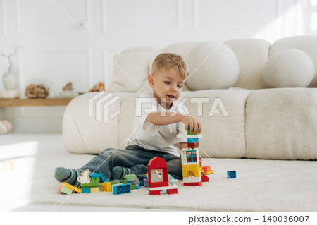 Young boy stacking colorful building blocks on a soft rug in a bright living room with a modern couch and decorative elements in the background Young boy stacking colorful building blocks on a soft rug in a bright living room with a modern couch and decorative elements in the background 140036007