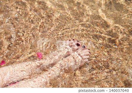 Women's feet with painted nails on the sand in clear sea water Women's feet with painted nails on the sand in clear sea water 140037040