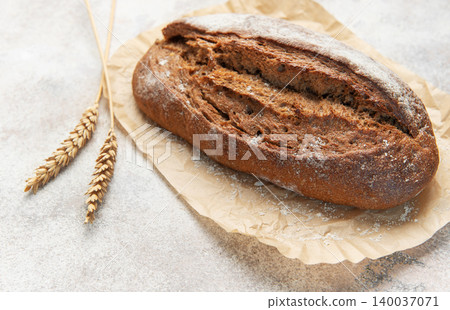 Rye bread loaf with wheat ears on parchment paper Rye bread loaf with wheat ears on parchment paper 140037071