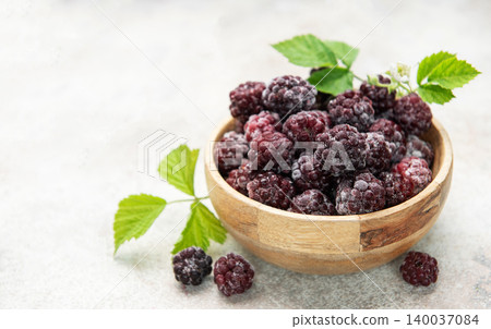 Frozen blackberries in wooden bowl with green leaves Frozen blackberries in wooden bowl with green leaves 140037084
