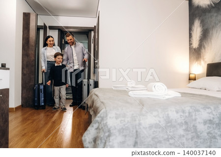 Family with luggage entering a modern hotel room featuring a neatly made bed, wooden flooring, and contemporary decor in a welcoming atmosphere Family with luggage entering a modern hotel room featuring a neatly made bed, wooden flooring, and contemporary decor in a welcoming atmosphere 140037140