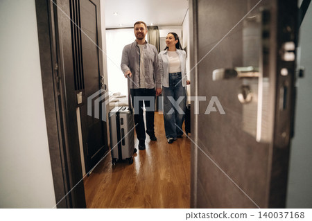 Couple entering a hotel room with a suitcase, smiling and enjoying their stay, modern interior design with wooden flooring and bright natural light Couple entering a hotel room with a suitcase, smiling and enjoying their stay, modern interior design with wooden flooring and bright natural light 140037168