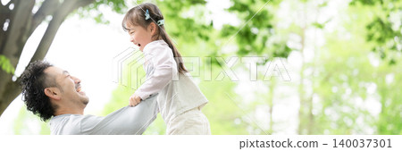 A heartwarming image of a family interacting and raising children, with a father and daughter playing in a park surrounded by fresh greenery, and a banner showing the father holding the daughter high in the air. 140037301