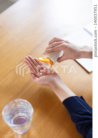 A close-up of a woman's hands as she takes a pill from a bottle. A close-up of a woman's hands as she takes a pill from a bottle. 140037951