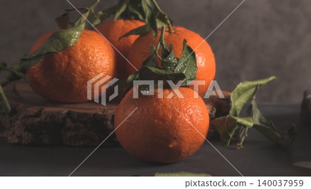 Fresh, wet tangerines with green leaves on a dark, rustic wood slice and stone background, featuring dramatic, low-key lighting Fresh, wet tangerines with green leaves on a dark, rustic wood slice and stone background, featuring dramatic, low-key lighting 140037959