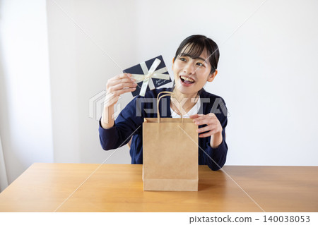 一位年輕的日本女子麵帶微笑，從明亮的房間裡的一個紙袋中取出一個禮物盒。 140038053