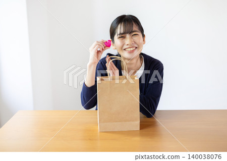 A young Japanese woman smiles as she takes a heart out of a paper bag in a brightly lit room. A young Japanese woman smiles as she takes a heart out of a paper bag in a brightly lit room. 140038076