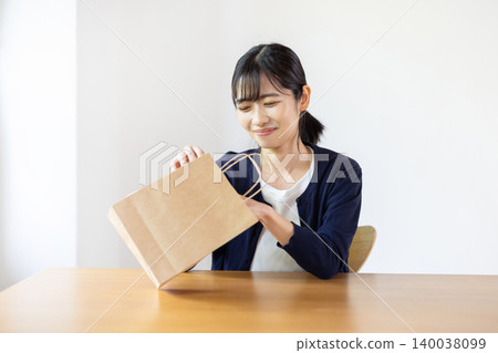 A young Japanese woman tries to check the contents of a paper bag in a brightly lit room. A young Japanese woman tries to check the contents of a paper bag in a brightly lit room. 140038099