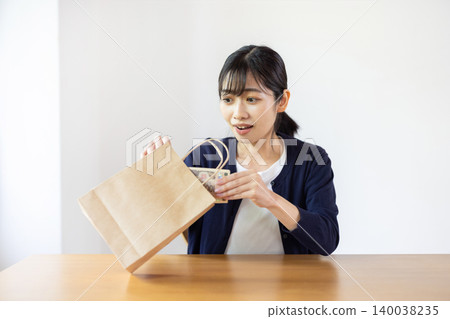 A young Japanese woman looks surprised as she takes a 10,000 yen bill out of a paper bag in a brightly lit room. A young Japanese woman looks surprised as she takes a 10,000 yen bill out of a paper bag in a brightly lit room. 140038235