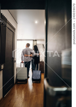 Couple standing in hotel room with luggage, embracing each other while looking at the interior design and furnishings of the modern accommodation Couple standing in hotel room with luggage, embracing each other while looking at the interior design and furnishings of the modern accommodation 140039070