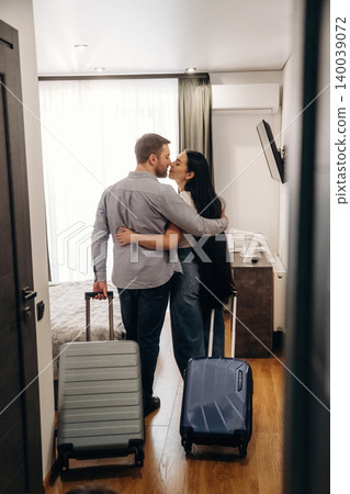 Couple embracing in hotel room with luggage, showcasing modern decor, bright natural light, and a cozy atmosphere, perfect for romantic getaways or travel experiences Couple embracing in hotel room with luggage, showcasing modern decor, bright natural light, and a cozy atmosphere, perfect for romantic getaways or travel experiences 140039072