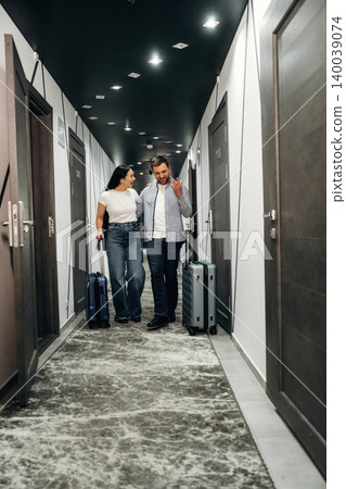 Couple walking in hotel corridor with luggage, modern doors and stylish lighting visible, showcasing contemporary interior design and travel experience Couple walking in hotel corridor with luggage, modern doors and stylish lighting visible, showcasing contemporary interior design and travel experience 140039074