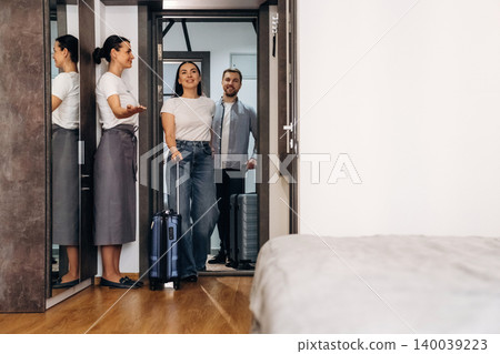 Hotel receptionist welcomes guests with luggage at the entrance of a modern room featuring a bed and stylish decor in a contemporary setting Hotel receptionist welcomes guests with luggage at the entrance of a modern room featuring a bed and stylish decor in a contemporary setting 140039223