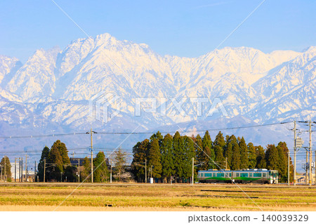 The magnificent scenery of the Ainokaze Toyama Railway 521 series train running through Toyama in early spring, with the snow-capped Tateyama mountain range in the background. The magnificent scenery of the Ainokaze Toyama Railway 521 series train running through Toyama in early spring, with the snow-capped Tateyama mountain range in the background. 140039329
