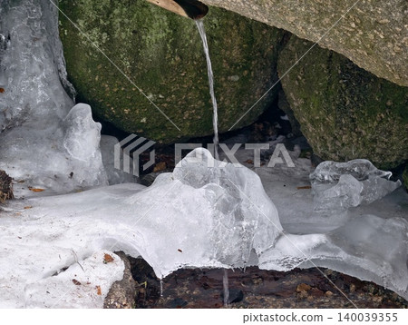 Close view of melting ice hanging from mossy stone showing delicate crystalline textures and winter light Close view of melting ice hanging from mossy stone showing delicate crystalline textures and winter light 140039355