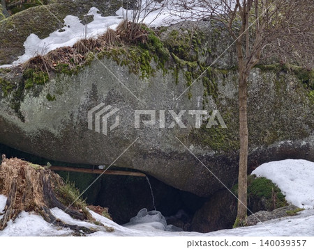 Snowy rocky shelter. Frozen cliffside overhang forming quiet refuge with patchy snow and exposed roots Snowy rocky shelter. Frozen cliffside overhang forming quiet refuge with patchy snow and exposed roots 140039357