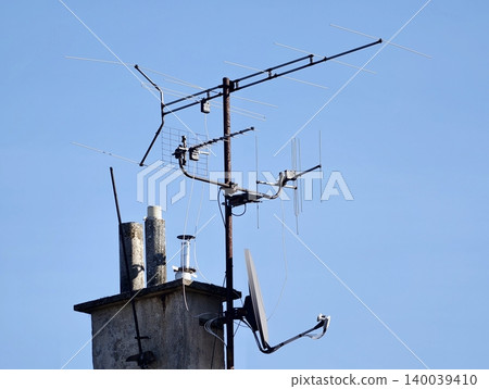 Weathered chimney with rooftop antenna. Broadcast equipment atop aged concrete chimney under clear sky 140039410