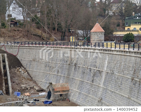 Individual engrossed in repairing city riverside wall with scaffolding and tools during overcast day 140039452