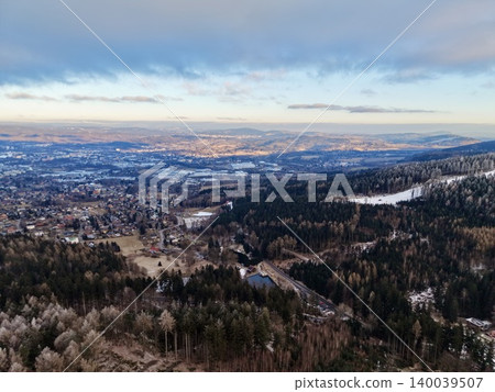 Frozen hill overlooks rural areas. Distant urban skyline merges with snowy landscape from icy ridge view Frozen hill overlooks rural areas. Distant urban skyline merges with snowy landscape from icy ridge view 140039507