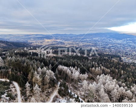 Snowy woodland panorama. Winter landscape with winding roads. Aerial view of snowy forest and distant town 140039510